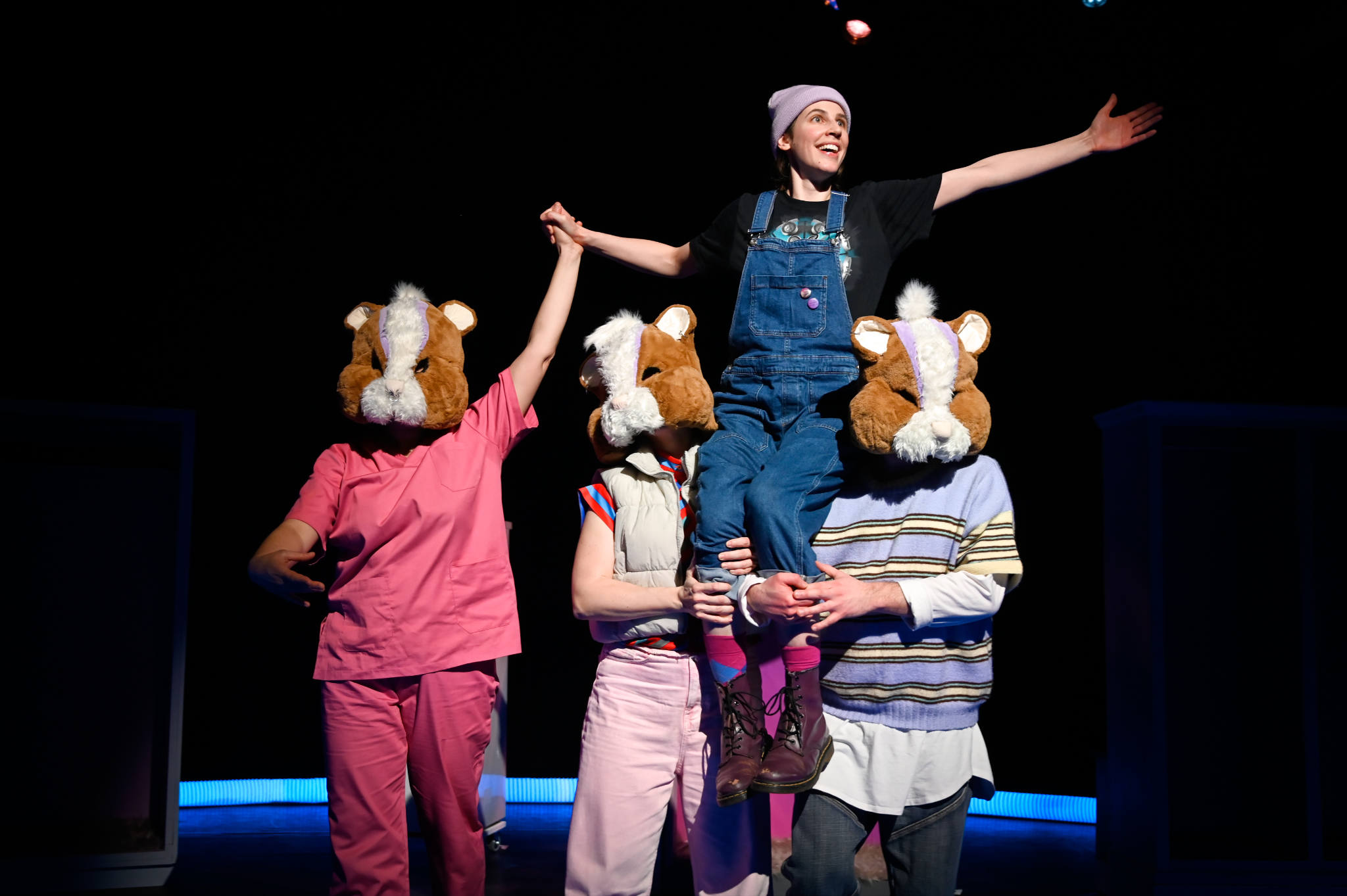 Drei Schauspieler*innen mit Hamstermasken tragen eine Schauspielerin.