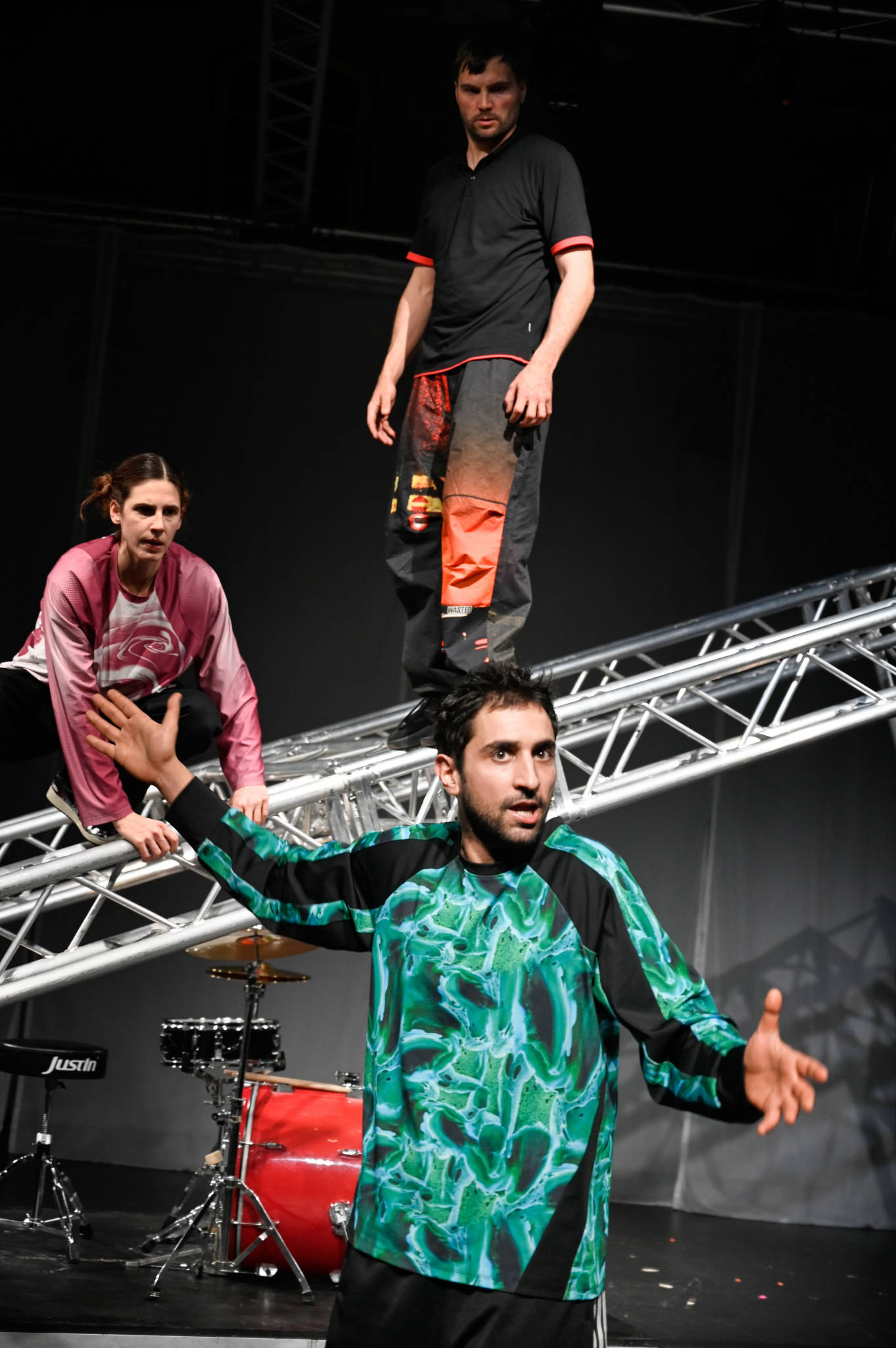 Drei Personen, eine restikuliert im Vordergrund, zwei dahinter stehen auf einem Gerüst.